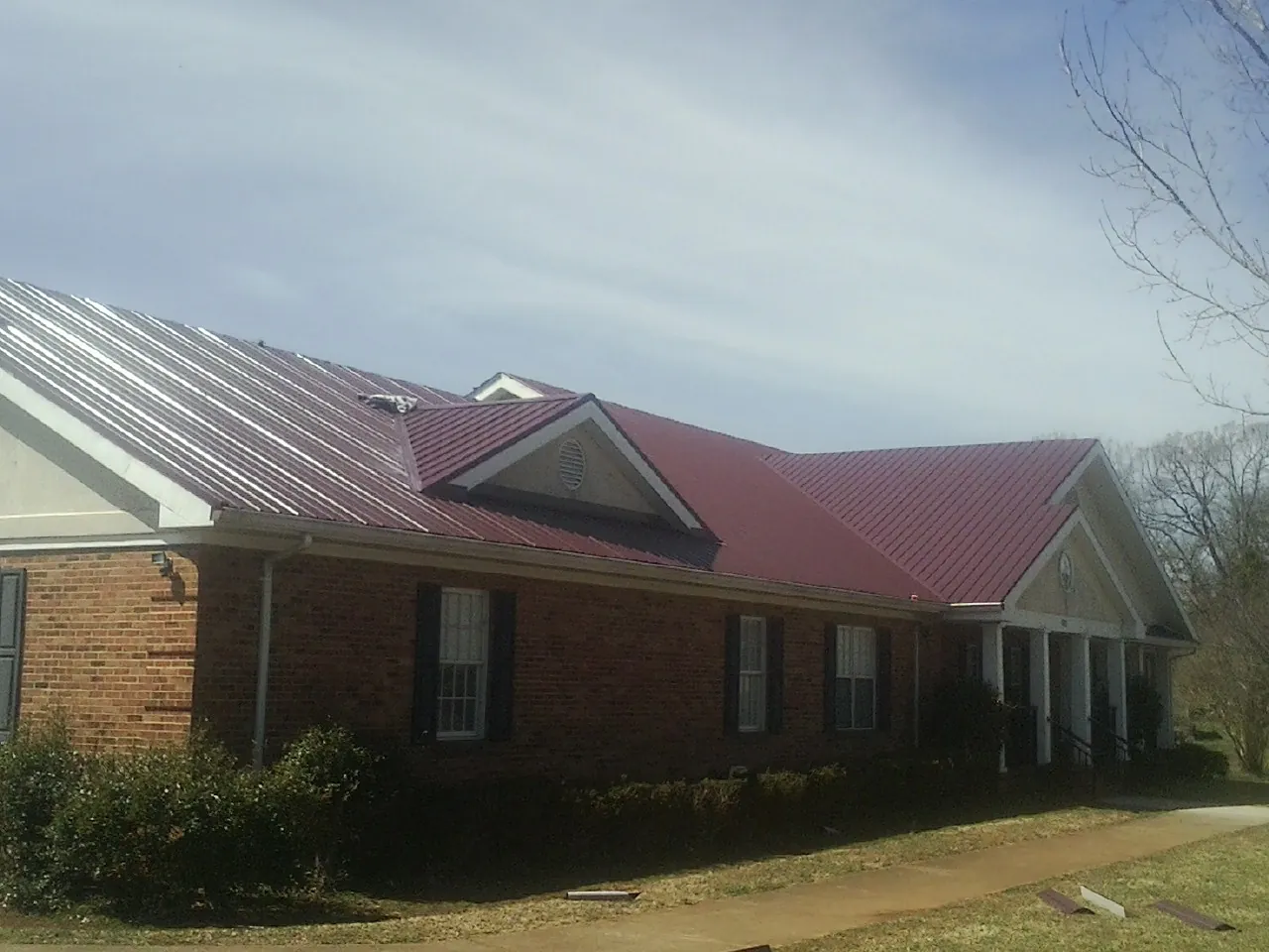 Red metal roof with gabled entries on a long brick building, from a Hail Damage Roof Repair job in Trimble