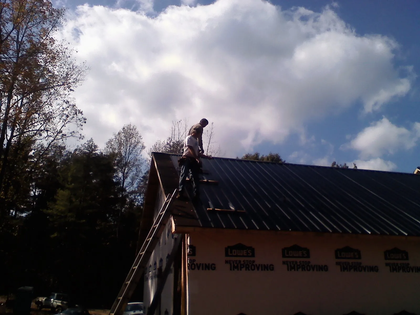 Roofer fastening dark metal panels high against a cloudy sky, from a Roof Inspection job in Trimble