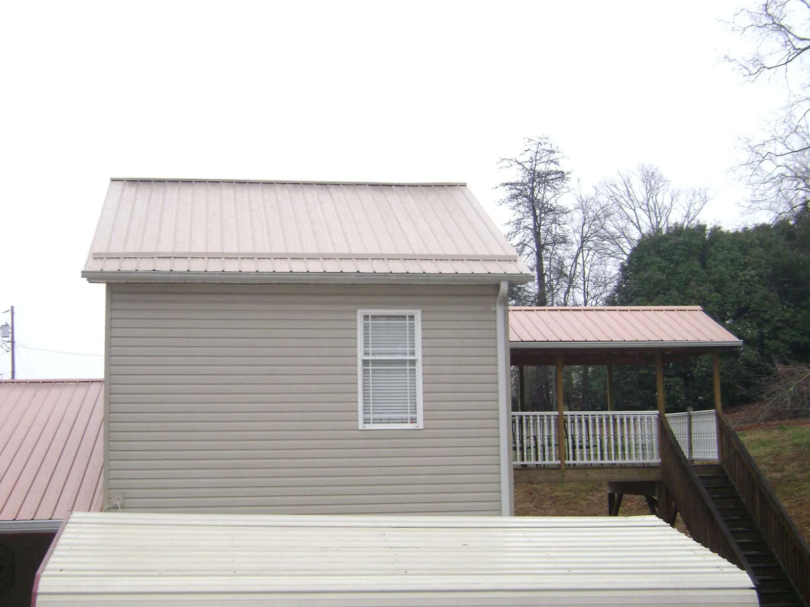 Tan metal roofs on a two story addition and attached porch, from a Roof Replacement job in Trimble